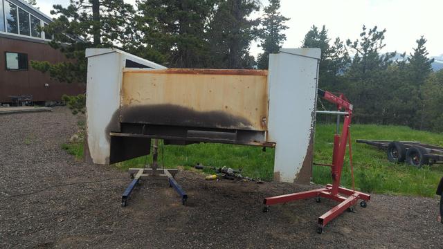 The service body from a 2007 GMC Sierra 2500HD. It's been removed and lifted about 3 feet in the air to allow the truck to drive out from underneath. Two engine hoists were used for this purpose, and are visible to either side.