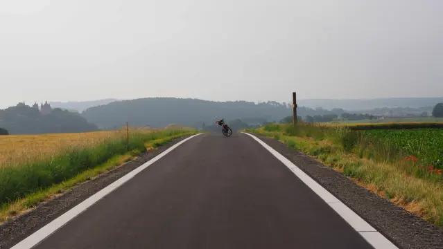 Neue breite Fahrradstraße mit weißen Streifen am Rand . In der Mitte der Straße steht ein Fahrrad und am linken Bildrand ist eine Burg zu erkennen
