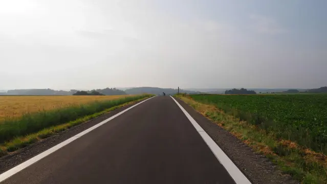 Neue breite Fahrradstraße mit weißen Streifen am Rand . In der Mitte der Straße steht ein Fahrrad und am linken Bildrand ist eine Burg zu erkennen