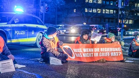 Abends sitzen vier Personen in Warnwesten auf einer Strasse, dahinter ein Polizeiauto. Auf einem Transparent das die jungen Menschen halten steht: "Was, wenn die Regierung das nicht im Griff hat?"