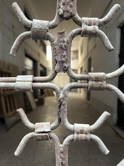 Looking through the cross of a security grille into an abandoned 20th Century industrial space on Leocharous, high-ceilinged and well-lit, clean and empty.