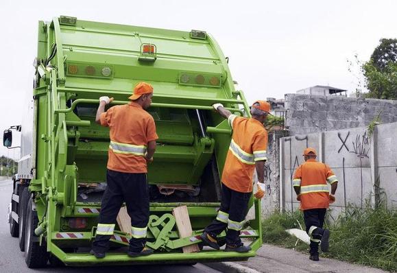 Trois éboueurs s'affairent auprès d'un camion-benne à ordures