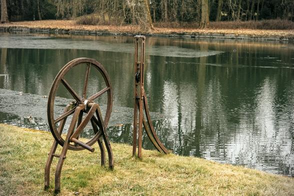 Sur la rive d’un cours d’eau, une roue en métal rouillée et un dispositif tout aussi rouillé
