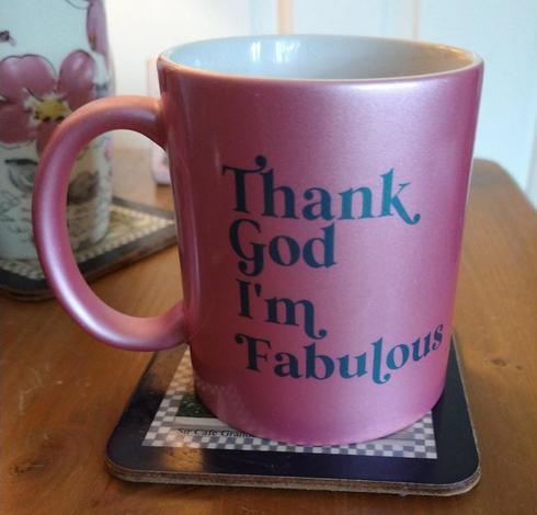 Pink mug of tea on a bedside cabinet with the words 'thank god I'm fabulous '