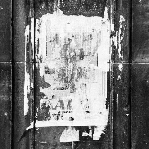 Square high contrast monochrome photo of a stone column, grooves running vertically at each side. Between is the remains of several bill posters, torn and faded now completely illegible but with a pleasing textured look