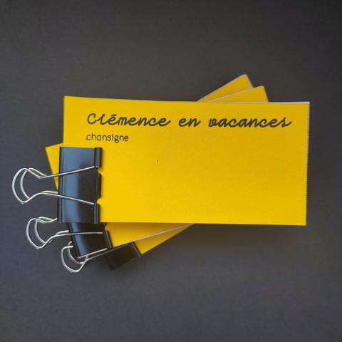 Photographie d'une pile de 3 éditions au format rectangulaire, une couverture jaune avec le titre 'Clémence en vacances' et le sous titre 'chansigne'. Une pince à dessin sert de reliure aux flipbooks.