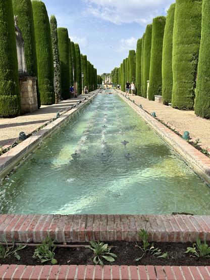A series of turquoise rectangular pools lined on both sides by manicured cypresses