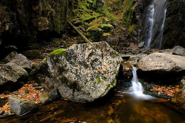 Detail view of the foot of Rainbow Falls, in New York state's Adirondacks region, dominated by a large central boulder on the edge of a shallow pool.