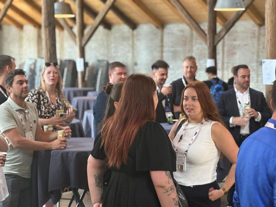 Attendees networking and chatting during a break at an Umbraco event inside a wooden-beamed venue.