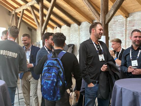 Attendees networking and enjoying coffee inside a rustic venue with wooden beams and high ceilings.
