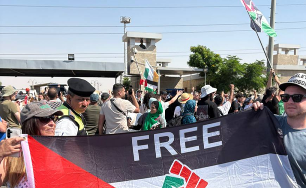 Zwei Personen halten am Kontrollpunkt Al-Ismailia eine "Free Palestine" Flagge, dahinter Soldaten und weitere Personen vor einem Grenzübergang
Foto: Global March to Gaza
