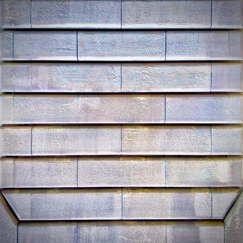 A sand-colored stone wall of large, horizontal bricks fills the frame, with a chamfered border carved into the bottom corners.