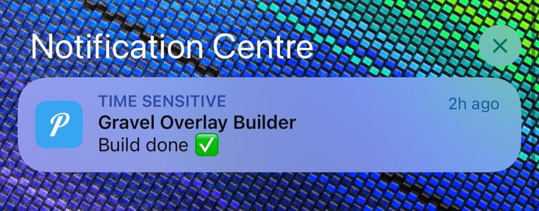 The image is a screenshot of an iOS notification. The background has a pattern of blue and green squares. The notification is from the Pushover app, which has a blue icon that has a white "P" in it. The text of the notification reads:

- "Notification Centre”
- "TIME SENSITIVE"
- "Gravel Overlay Builder"
- "Build done" with a green checkmark next to it.

The notification was sent "2h ago" (2 hours ago). There is also a small "X" in the top right corner, likely indicating a button to dismiss the notification.