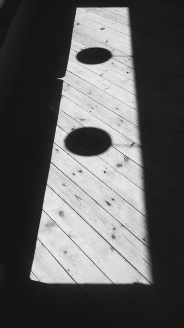 A rectangle of bright sunlight on a wooden floor, surrounded by shadows, with the silhouette of two globe shaped lamps in the middle