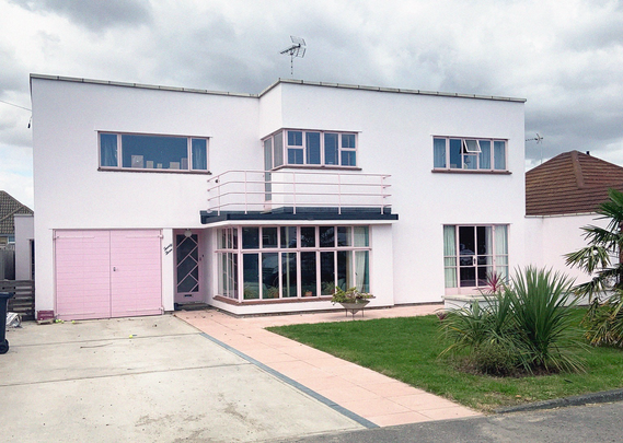 A colour photograph of a pink-painted modernist house on the Frinton Park estate
