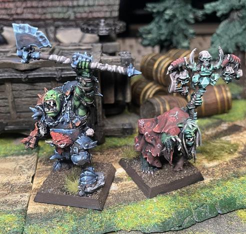 An orc warboss in plate mail, lifting a gigantic axe above his head single handedly, painted in something resembling non metallic metals.

And an orc witch in tattered red robes, arcane sigils scrawled in random patterns across them. A glowy green stone at the centre of the staff she’s heavily leaning upon, and fingers outstretched toward her next cursed target.