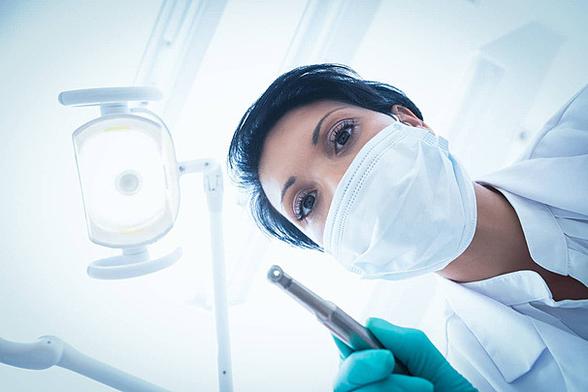 Color image of a dentist with a dental drill, from the viewpoint of the patient looking up at the dentist.