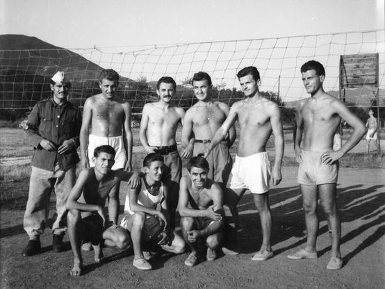 A row of men pose shirtless. The postcard is black and white and the men are all conventional attractive.
