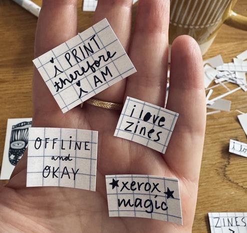 a hand holding stickers that say: offline and okay, xerox magic, i love zines, i print therefore i am.