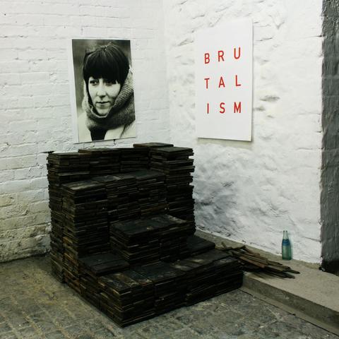 The original cover of Brutalism from Idles which shows what looks like an art exhibition with a stone wall, a black and white photo of a woman and a square with the word BRUTALISM in three rows, in red font over a white background