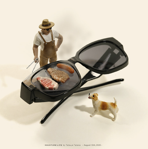 The image features a miniature scene with a pair of oversized black sunglasses as the central element. Inside the lenses, there are three pieces of meat: a steak, a sausage, and a grilled piece of meat. To the left of the sunglasses, a small figurine of a man wearing a white shirt, brown overalls, and a hat is holding a pair of tongs, seemingly grilling the meat. To the right of the sunglasses, a small dog figurine with a white and brown coat is standing and looking towards the man. The background is a plain, light-colored surface, and the overall composition is playful and whimsical. The text at the bottom reads "MINIATURE LIFE by Tatsuya Tanaka - August 13th, 2023 -".

Provided by @altbot, generated privately and locally using Ovis2-8B
