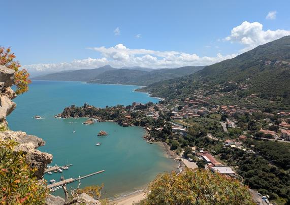 Questa foto mostra il versante orientale di Cefalù, visto dall’alto della Rocca, con uno sguardo che abbraccia il piccolo porto turistico e l'insenatura nascosta dietro la Rocca di Cefalù.

In basso a sinistra si vede il porticciolo con alcune barche ormeggiate, protetto da un molo. L’acqua è di un azzurro turchese intenso, che contrasta con i rilievi verdi e le colline che si innalzano sulla destra. Spiccano anche alcune rocce isolate affioranti dal mare