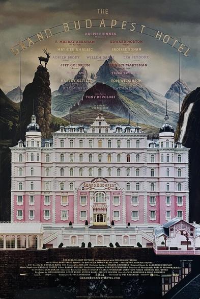 The Grand Budapest Hotel en letras de molde sobre paisaje con montañas y un hotel blanco con rosado. 
Abajo los créditos en letras pequeñas.