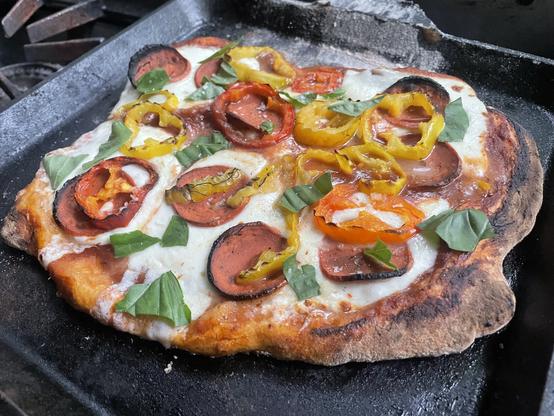 A somewhat misshapen (but fresh and hot) sourdough pizza with fake pepperoni, banana peppers, and basil.