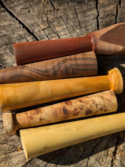 Sur un billot de bois au soleil de fin de journée, cinq morceaux de bois coniques, avec des teintes très différentes.