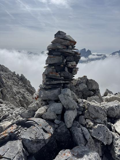 Cairn on summit of Piz digl Gurschus. Clouds and summit of Piz Forbesch in the background.