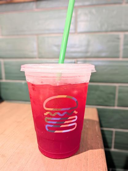 Plastic Shake Shack cup with their Pride flag- colored logo, filled with cherry limeade