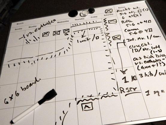 Calendar white board with rectangular spaces used to plot out a gridded board for the Battle of Great Bridge, with notes on units (artillery and infantry) and starting locations, movement, and hit chances, all scrawled in black dry-erase marker like the ravings of a madman....