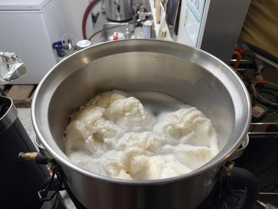 Pillowy foam from the yeast fermentation on the top of a round stainless steel fermentation vessel
