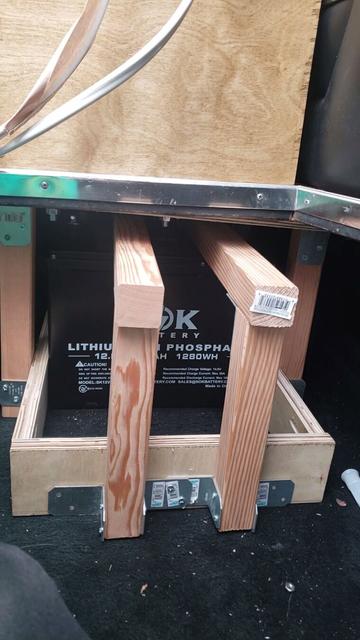 A LiFePO4 battery is mounted in a wooden cage, reinforced in some areas by metal plates.