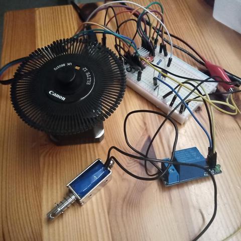 Messy electronics prototyping - daisy wheel from a Canon printer mounted to a stepper motor, solenoid triggered by a relay, motor driver on a breadboard