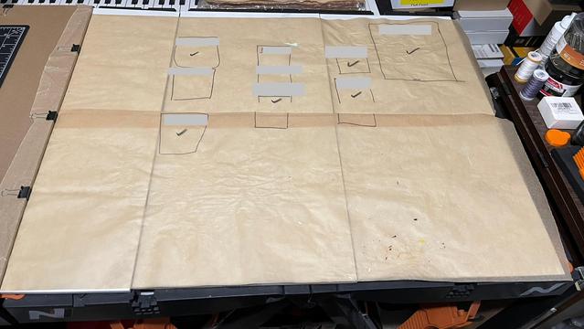 The top of a portable workbench which has two pieces of 12 inch wide parchment paper on top of it to cover the full 24 inch surface. 

There are sharpie marks on the parchment paper