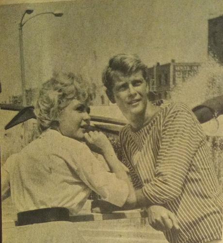 Sandra Dee y pretendiente posando juntos en un entorno urbano, con una expresión relajada y sonriente.