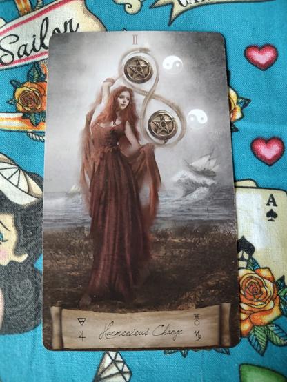 Card from the Heaven and Earth Tarot deck. 
Two of Pentacles. 
A woman in red dress, who also happens to be a redhead, is balancing and twirling two large pentacles.