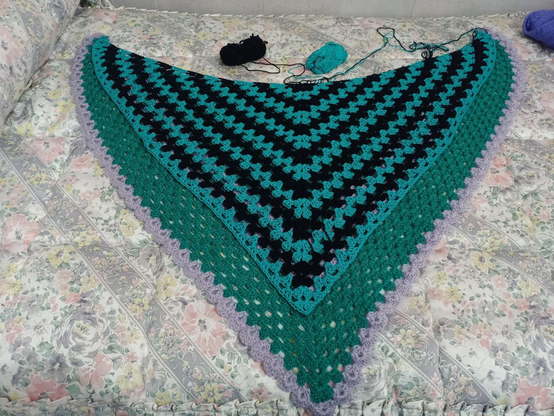 Emochal, de algodón verde azulado y negro alternando franjas en forma de V, sobre Protochal, de lana sintética mayormente verde con un par de franjas lila en V y también el remate en abanicos.
Emochal ha crecido tanto que ya tapa por completo las franjas lilas.