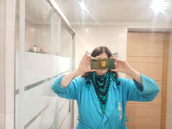 Selfie sacada en el espejo del baño, anonimizada por taparme la cara con el móvil.
Me he echado a Emochal en torno al cuello, con el pico central sobre el pecho y los picos laterales cayendo un palmo a ambos lados