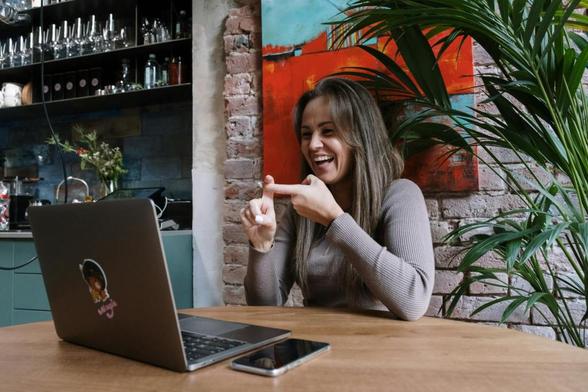 woman in gray sweater sitting by the table doing hand sign while having video chat