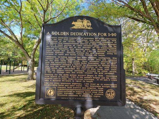 Photo of a sign along a bike trail, titled "A Golden Dedication For I-90" along with several paragraphs of historical information.