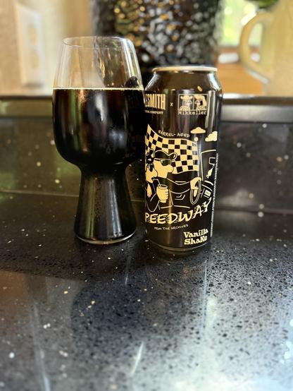 A stout glass full of dark beer is to the left of a black pint can with tan lettering and a checkerboard flag