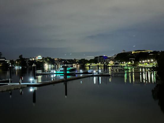 Looking down a reach of the Brisbane river some time before dawn. In the foreground are a series of private moorings, mostly empty save for one stinkboat with lurid green stern lighting. Down the right bank are the serried lights of the riverwalk, on the left bank, random houses and other buildings are lit up. The river is calm, reflecting all the lights, and the sky is (choose your poet/author stretched out like a patient etherised (eliot) / the colour of television tuned to a dead channel (gibson))