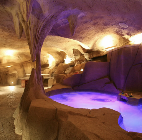 An underground cave with lighting and a purple lighted up hot tub.