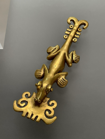 photo of the gold crocodile pendant on display at museum, top down view, stylized with forked tail and ornamental plate in mouth