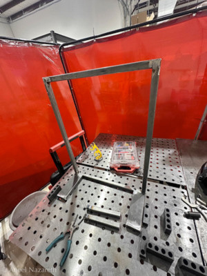 A partly-welded metal frame on a fixture table with various fixtures used to hold things in place
