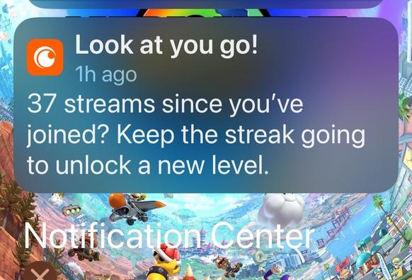 A notification on a smartphone screen congratulating the user for completing 37 streams since joining, encouraging them to keep the streak going to unlock a new level. The background features a colorful animated scene, likely related to gaming.