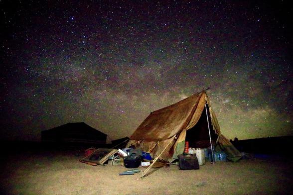 An old army tent in the foreground is illuminated by the milky way in the distance.