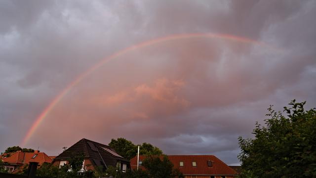 Foto eines relativ rötlichen Regenbogens vor einem wolkigen Himmel.